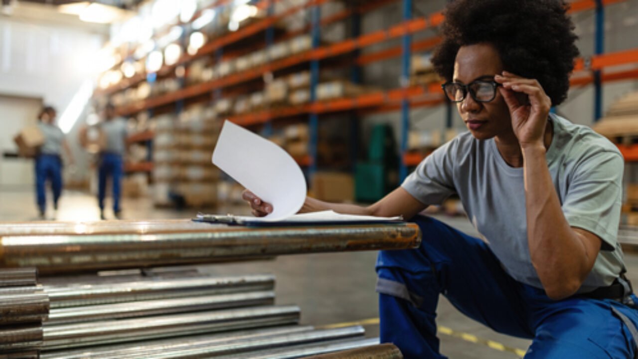Black female warehouse worker examining check list before the distribution.