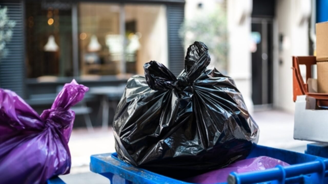 Purple and black bags of trash on a garbage bin during daytime