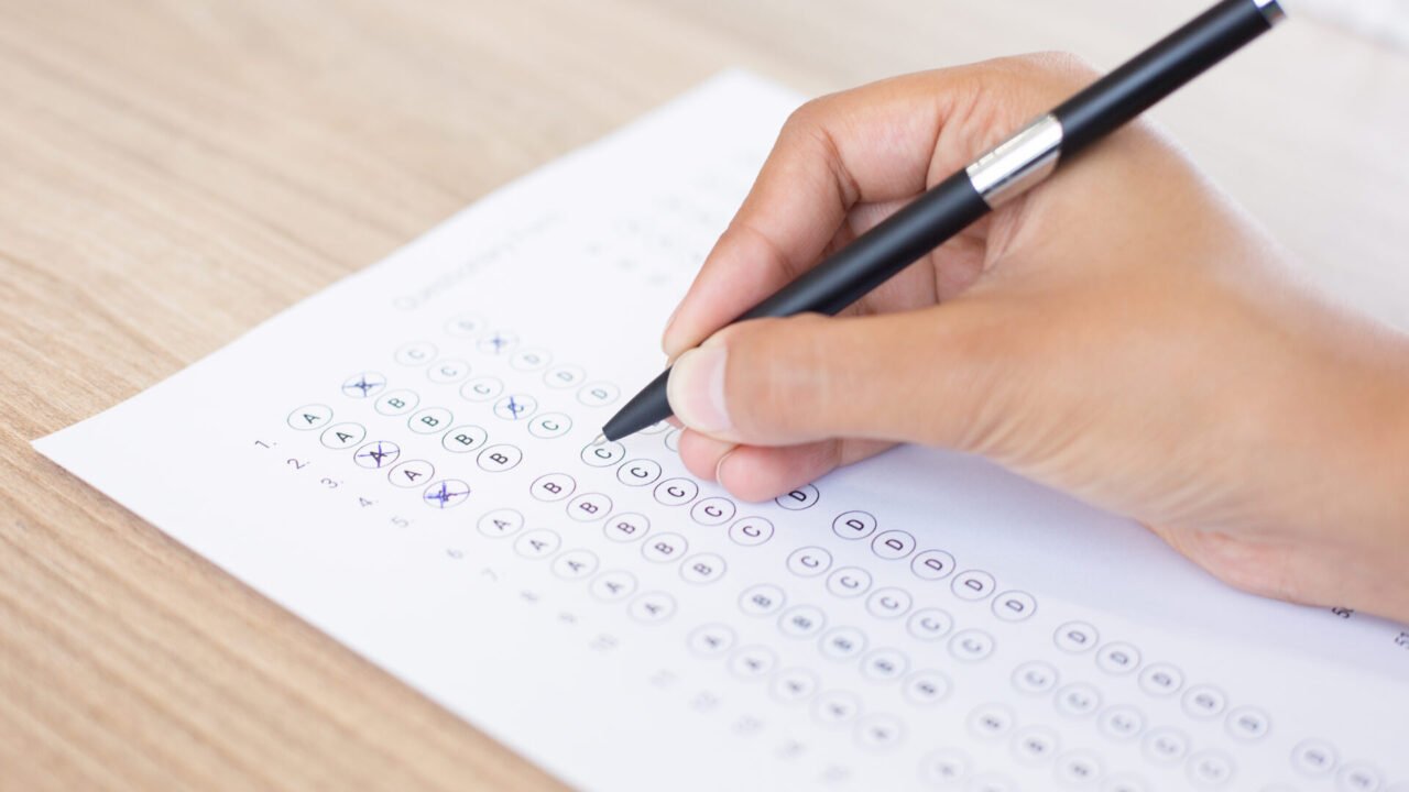 Closeup of hand holding pen and filling out questionary form on table