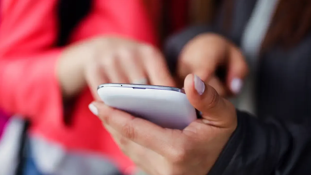 two-beautiful-students-using-mobile-phone-street_0